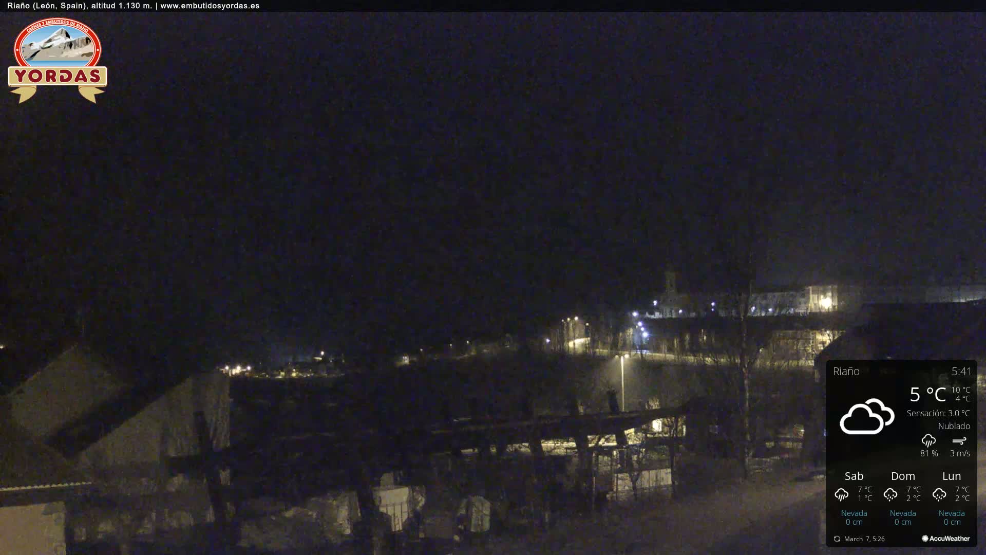 A nighttime view of a town under cloudy skies, with a few lights visible.