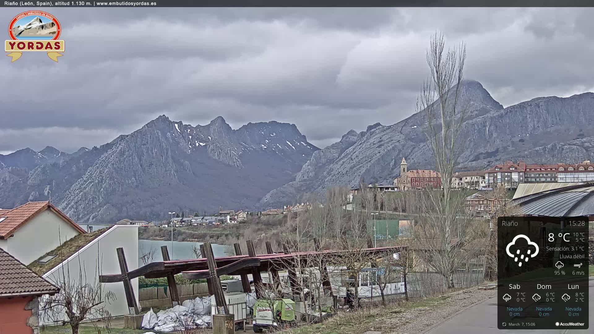 A town nestled in a valley between snow-capped mountains under a cloudy, drizzly sky.