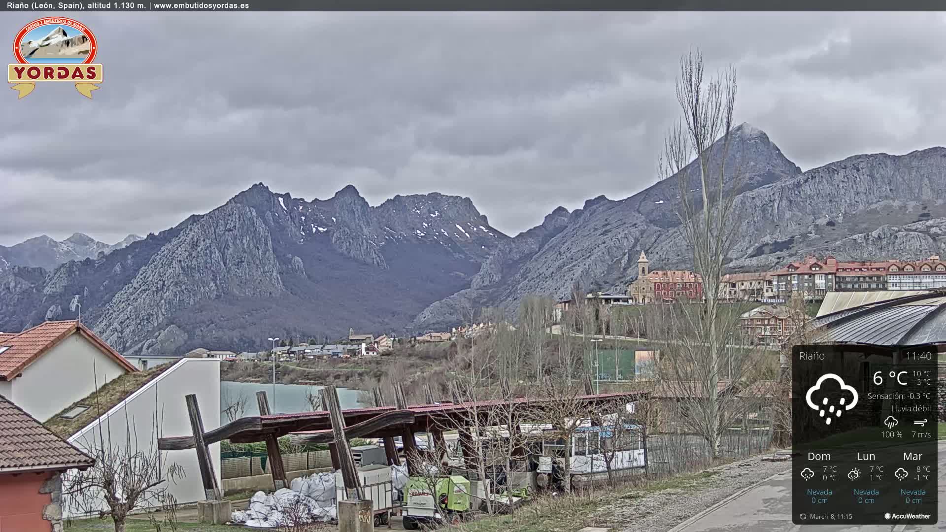 A town nestled in a valley between snow-dusted mountains under a cloudy, rainy sky.