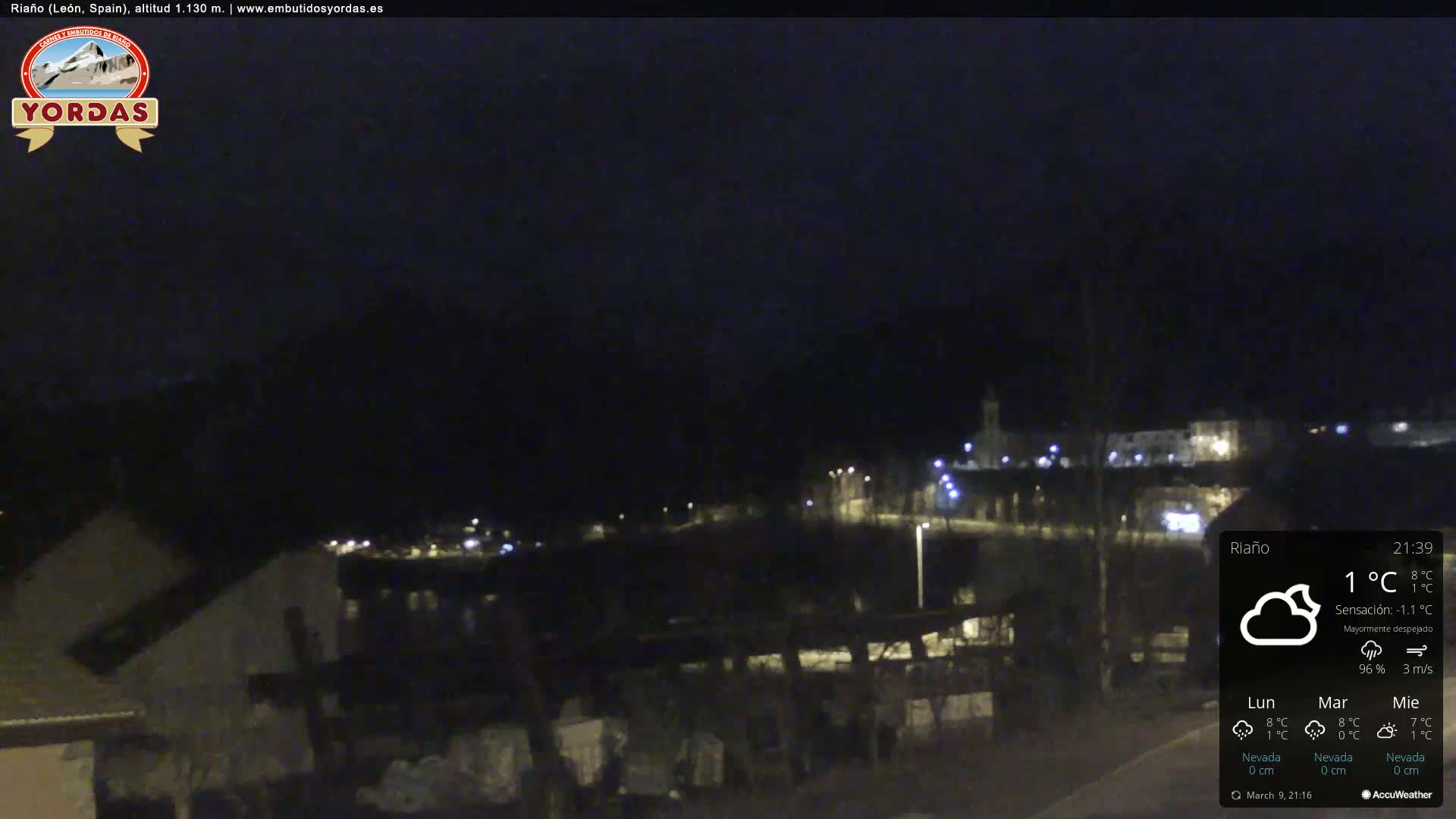A nighttime view of a dimly lit town nestled in a valley, under a mostly clear sky with a temperature of 1°C.