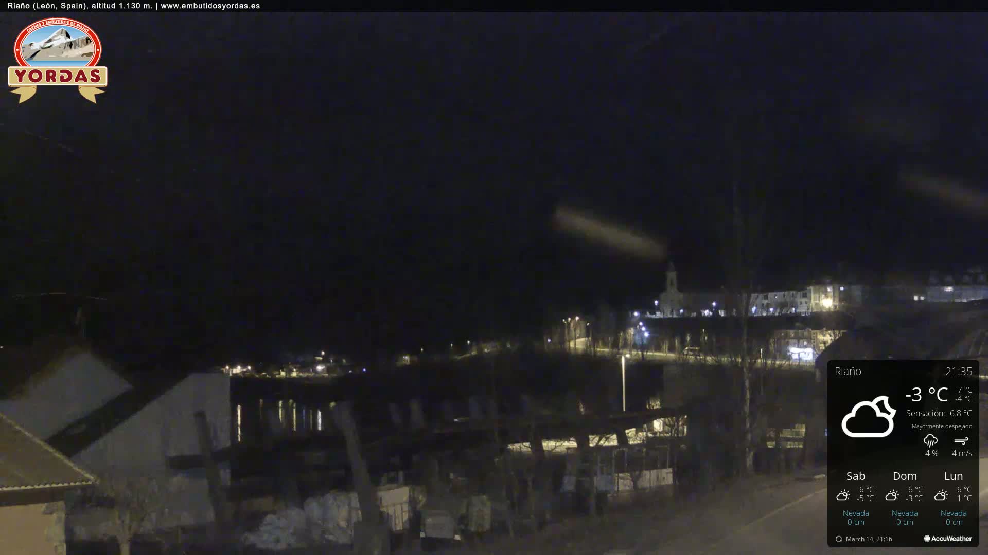 A nighttime view of a small town, illuminated by scattered lights, under a mostly clear sky with a temperature of -3°C.
