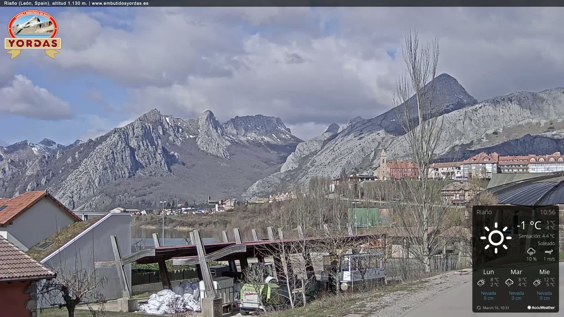 A partly cloudy day reveals a town nestled in a valley between imposing, snow-dusted mountains.