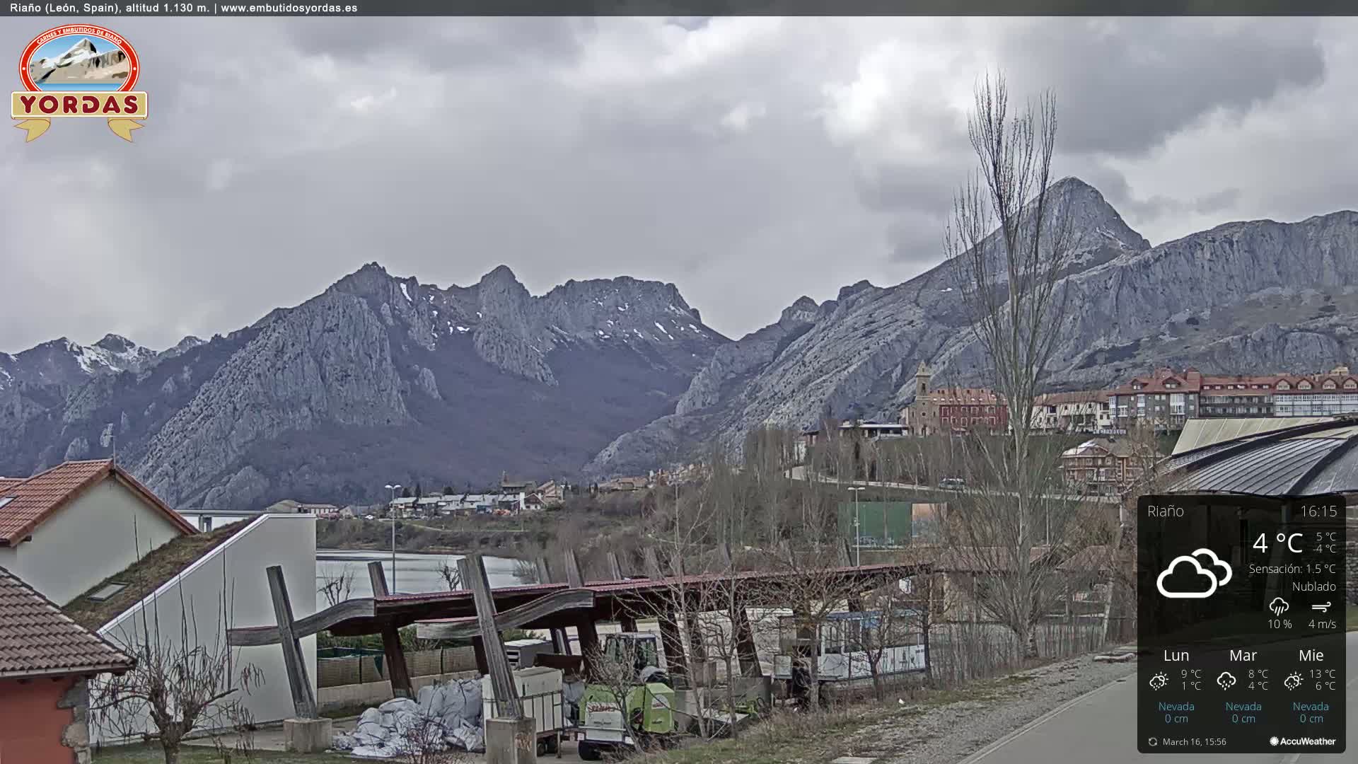 A cloudy day reveals a town nestled at the base of a large, snow-capped mountain range.