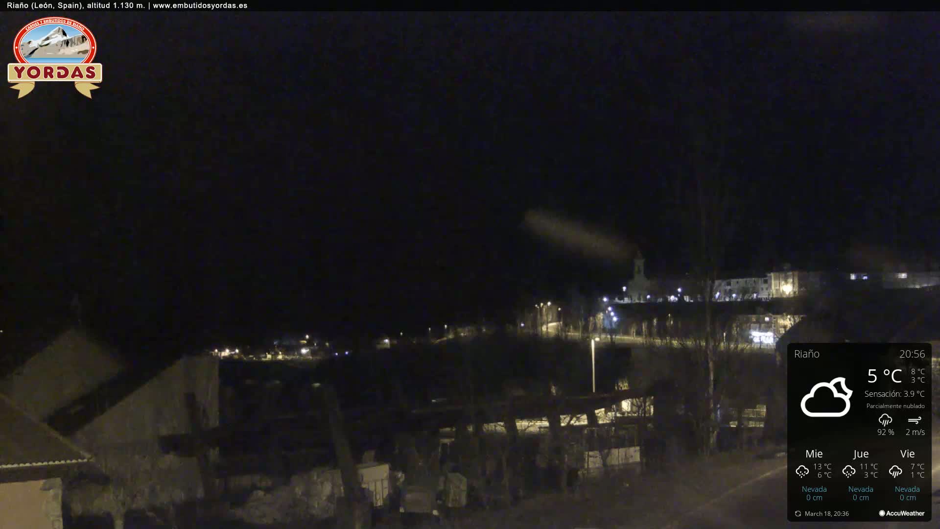 A nighttime view of a small town with sparsely lit buildings under a partly cloudy sky.