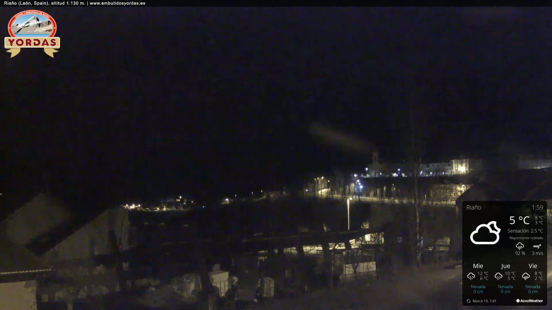 A nighttime view of a small town, mostly obscured by darkness, under a mostly cloudy sky.