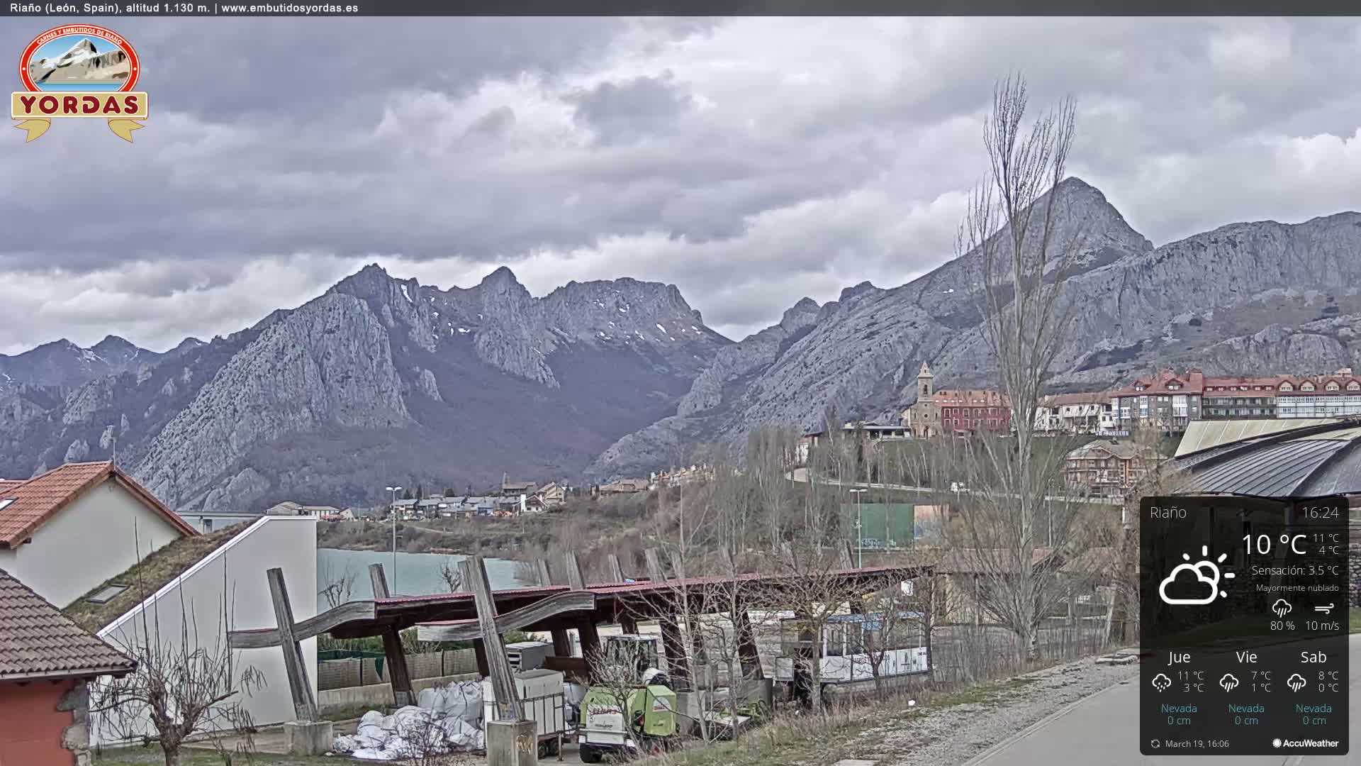 A village nestled in a valley between large, gray mountains under a mostly cloudy sky.