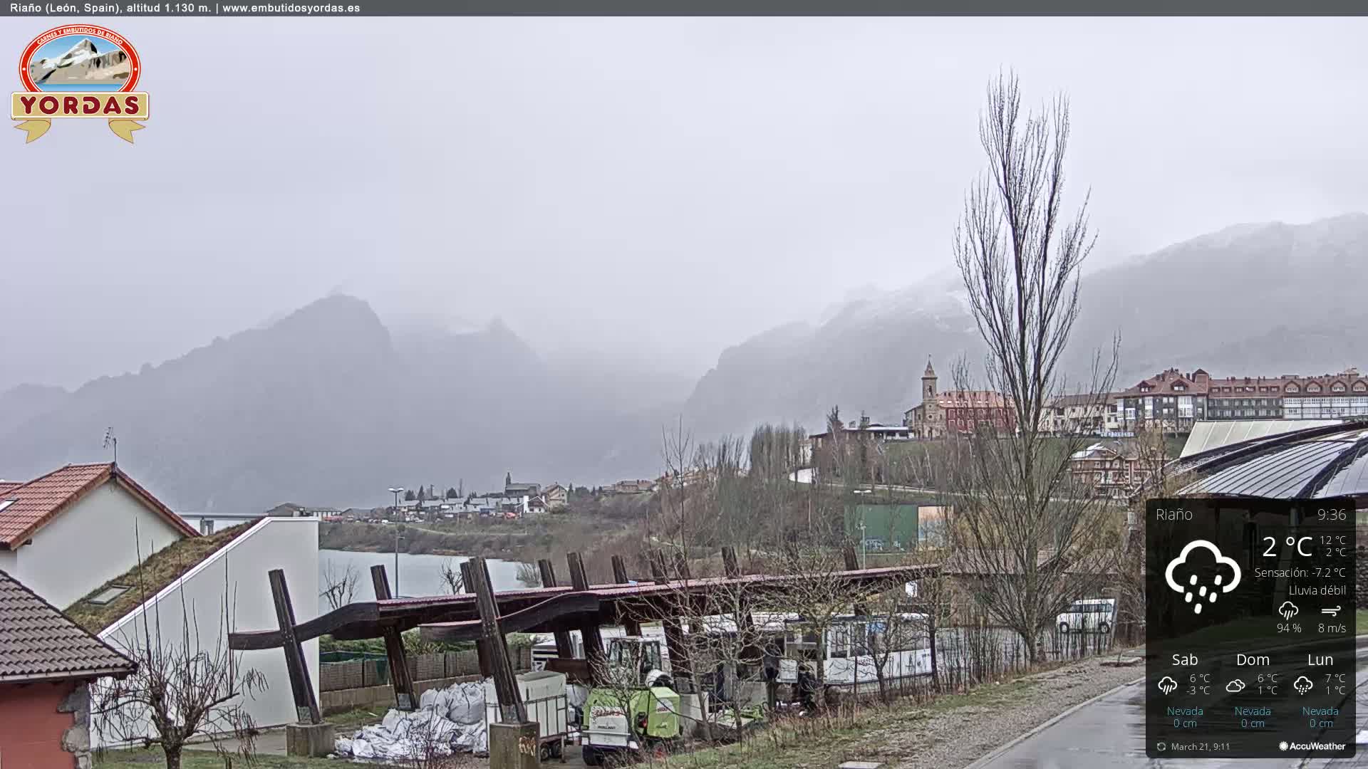 A village nestled in a valley between misty mountains under a light rain.