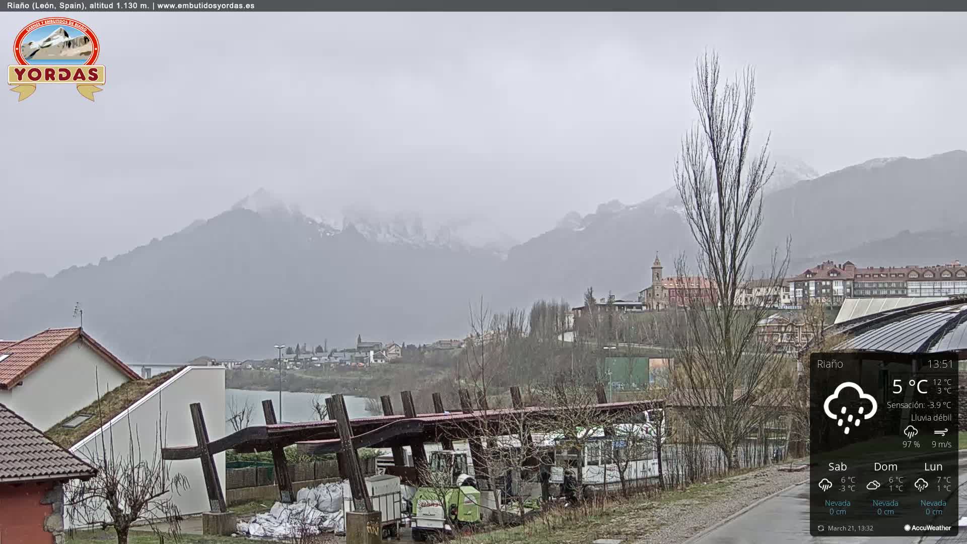 A view of a town nestled in a valley between snow-capped mountains on a cloudy, rainy day.