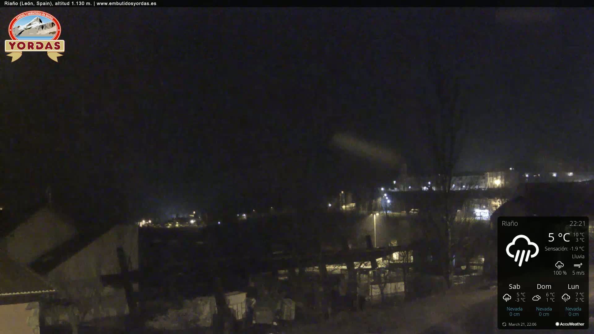 A nighttime view of a town under heavy rain, with a few lights visible in the distance.