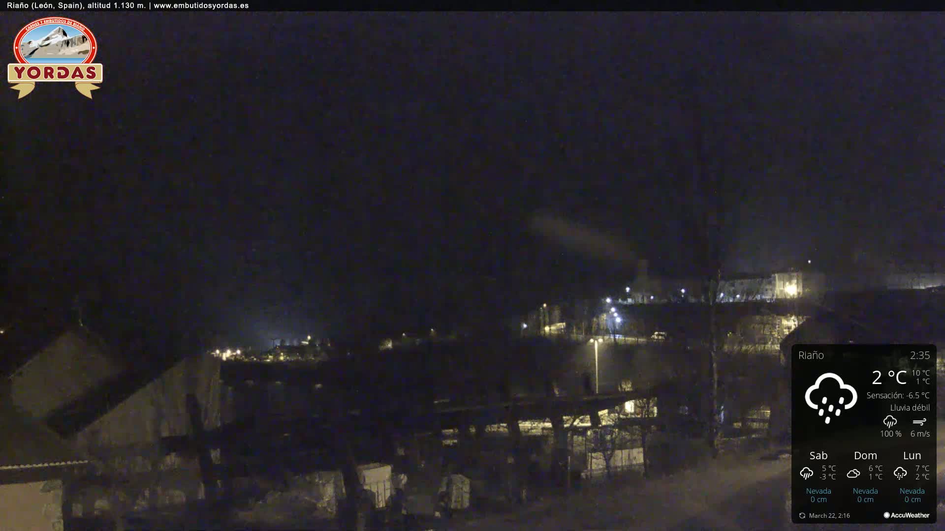A nighttime view of a snow-dusted town under a dark sky with light rain.