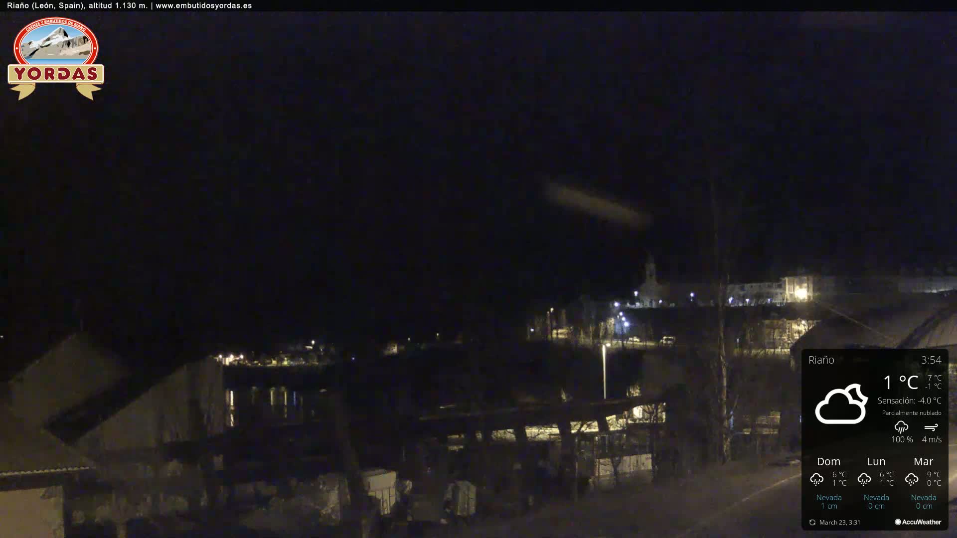 A nighttime view of a town partially obscured by darkness and partly cloudy conditions, with a few lights visible.