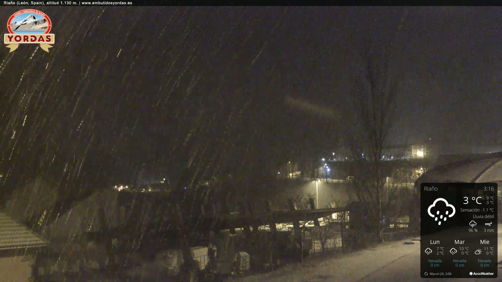 A nighttime scene of snow falling over a town, illuminated by streetlights.
