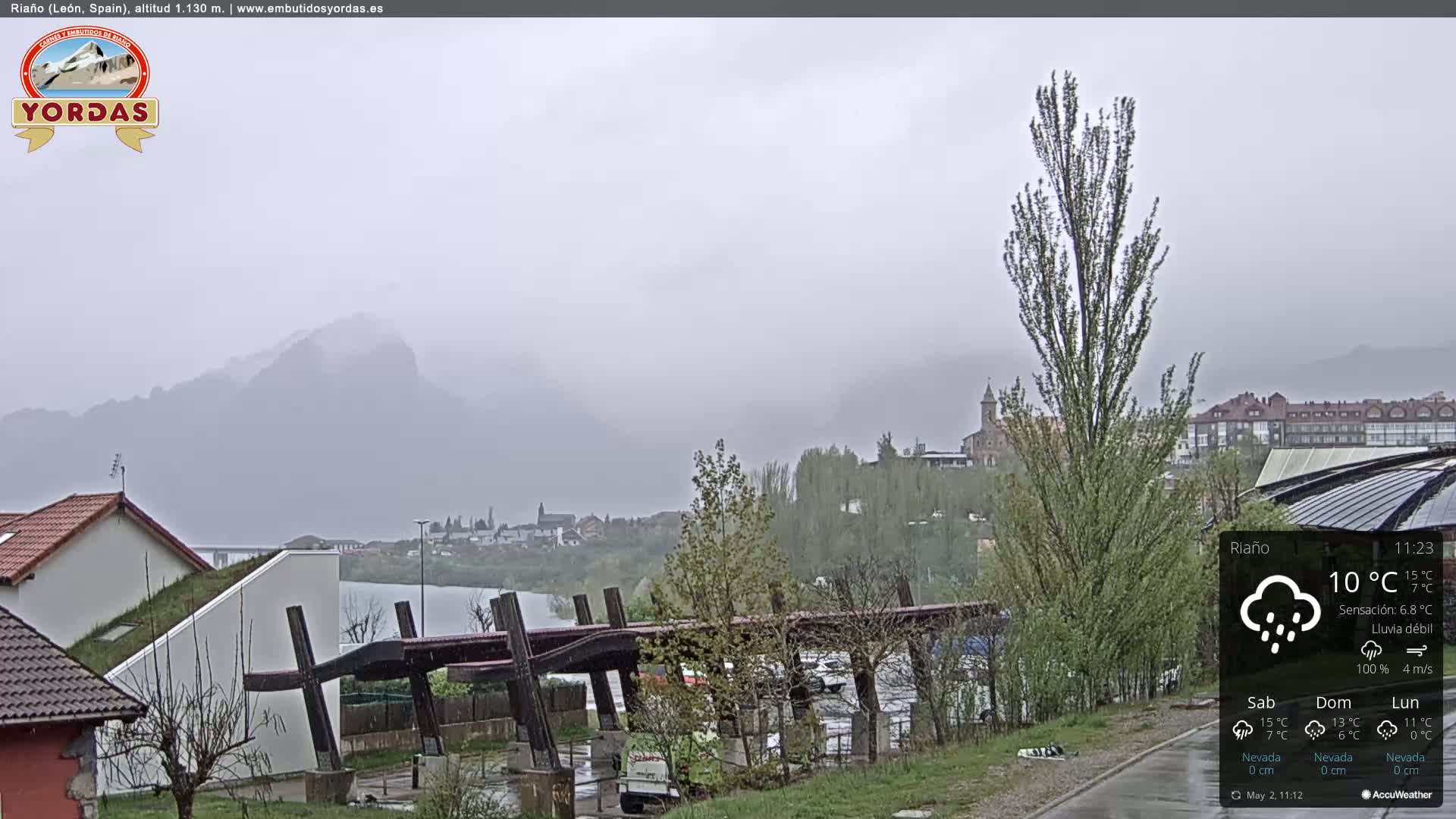 A hazy, rainy view of a town nestled between mountains and a lake, with a modern structure in the foreground.
