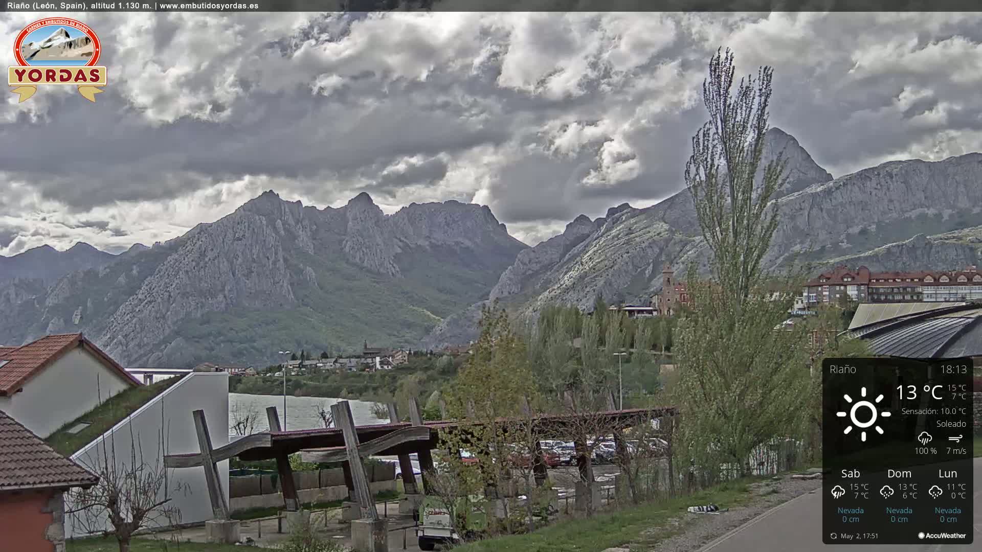 A mountain range is visible under a mostly cloudy sky, with a town and some buildings situated in the foreground.