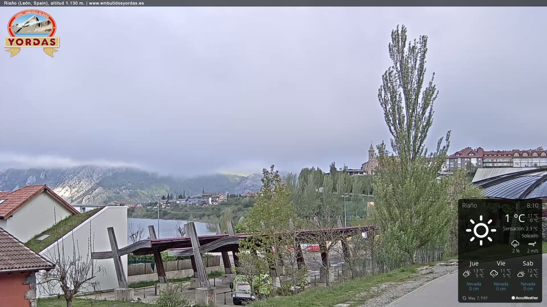 A partly cloudy day reveals a town nestled beside a lake and mountains shrouded in fog.