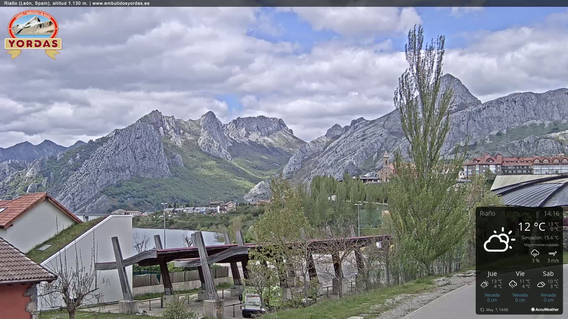 A partly cloudy day reveals a town nestled at the foot of a range of gray, rocky mountains.