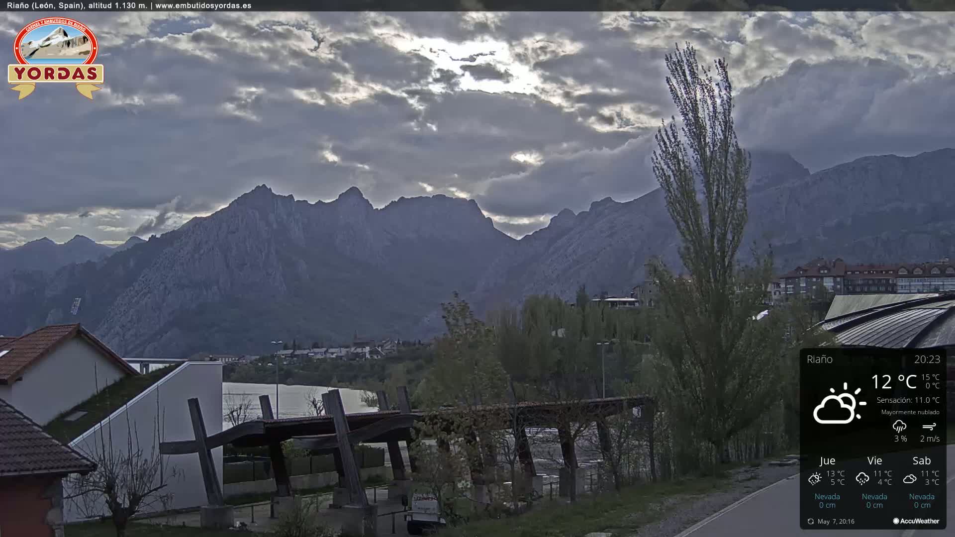 A mostly cloudy view of a town nestled at the foot of a mountain range.