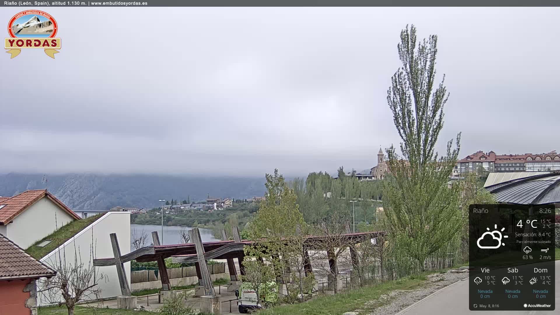 A partly sunny, overcast view of a town nestled beside a lake and mountains, with some fog in the distance.