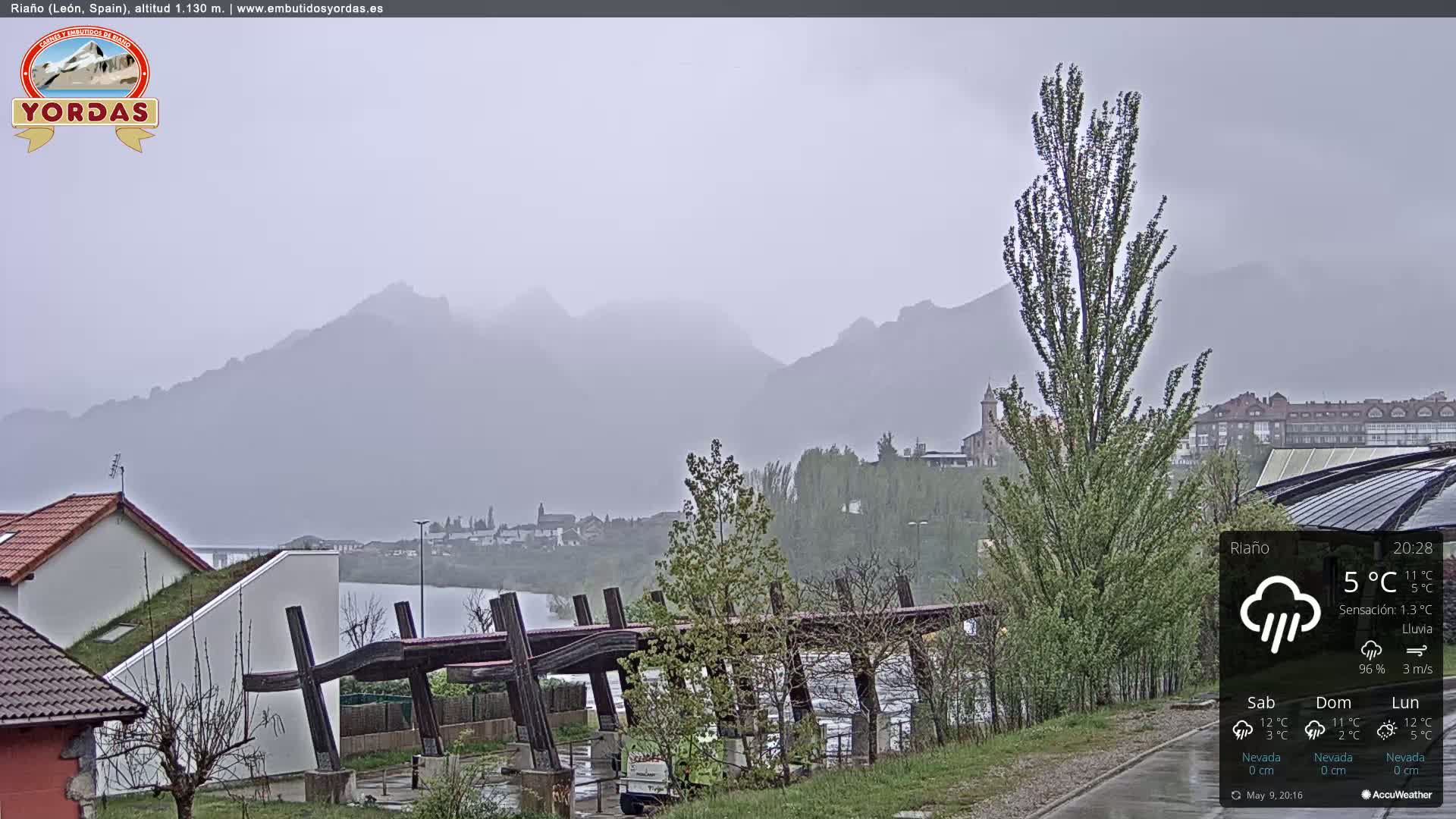 A misty, rainy view of a town nestled beside a lake and mountains.