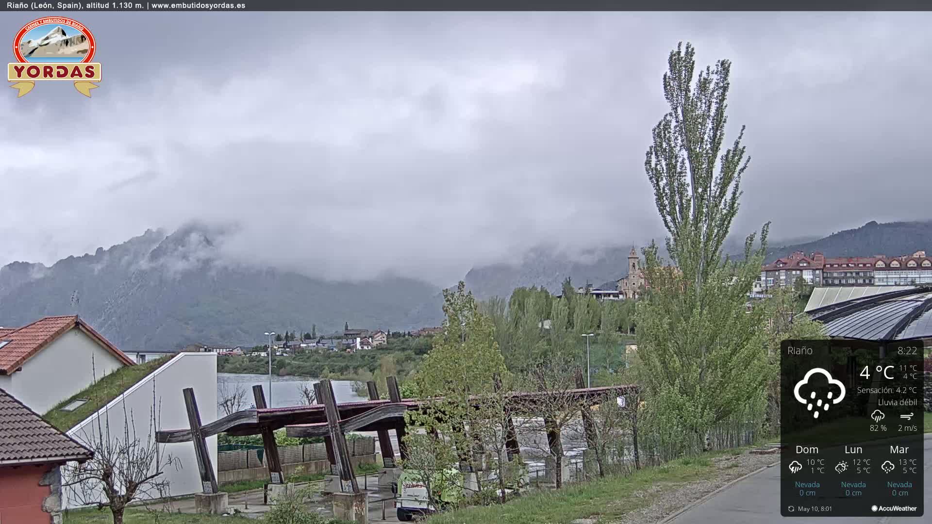 A misty, overcast day reveals a town nestled in a valley between mountains, with light rain falling.