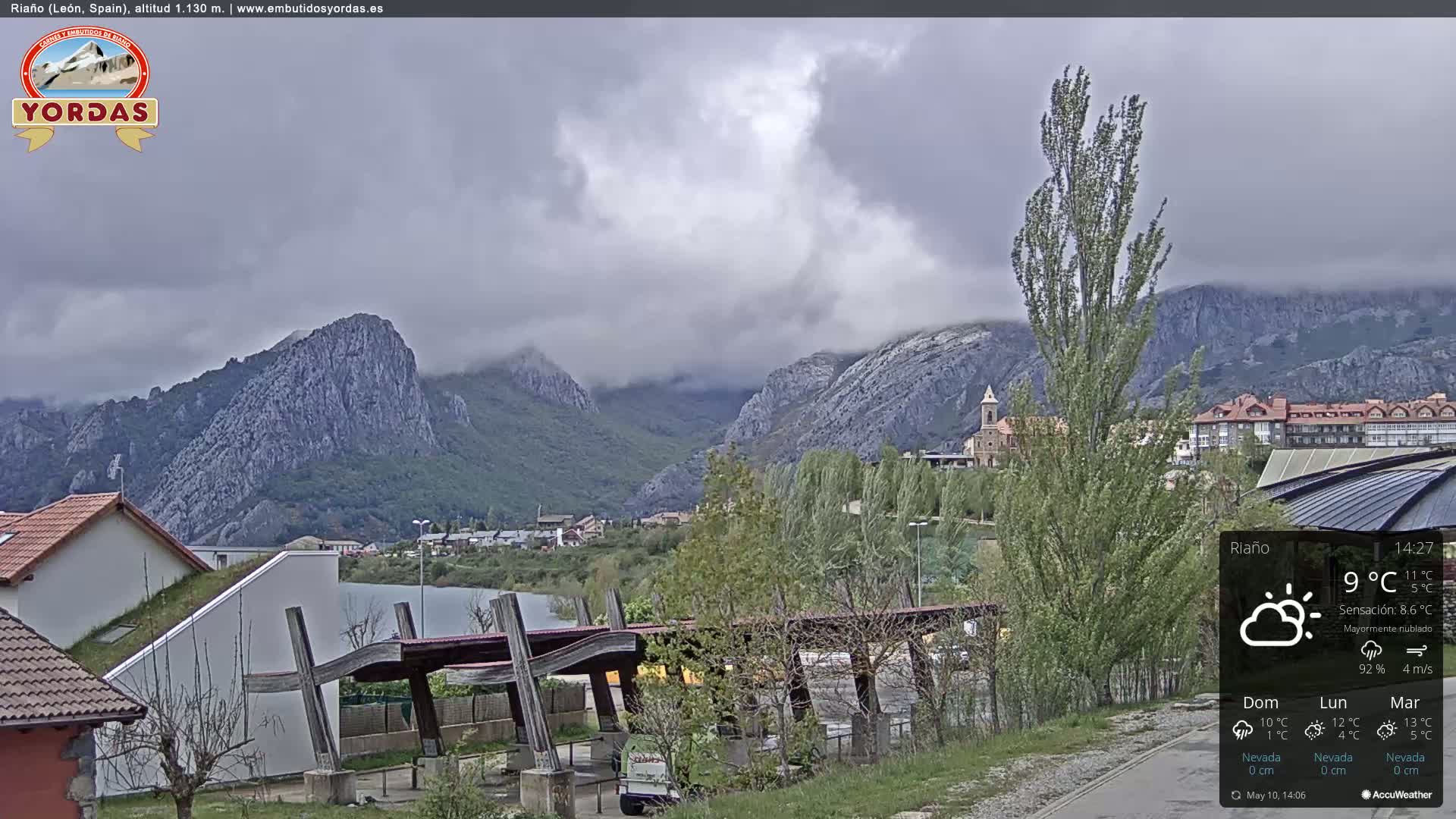A mostly cloudy view of a town nestled in a valley between rocky mountains.