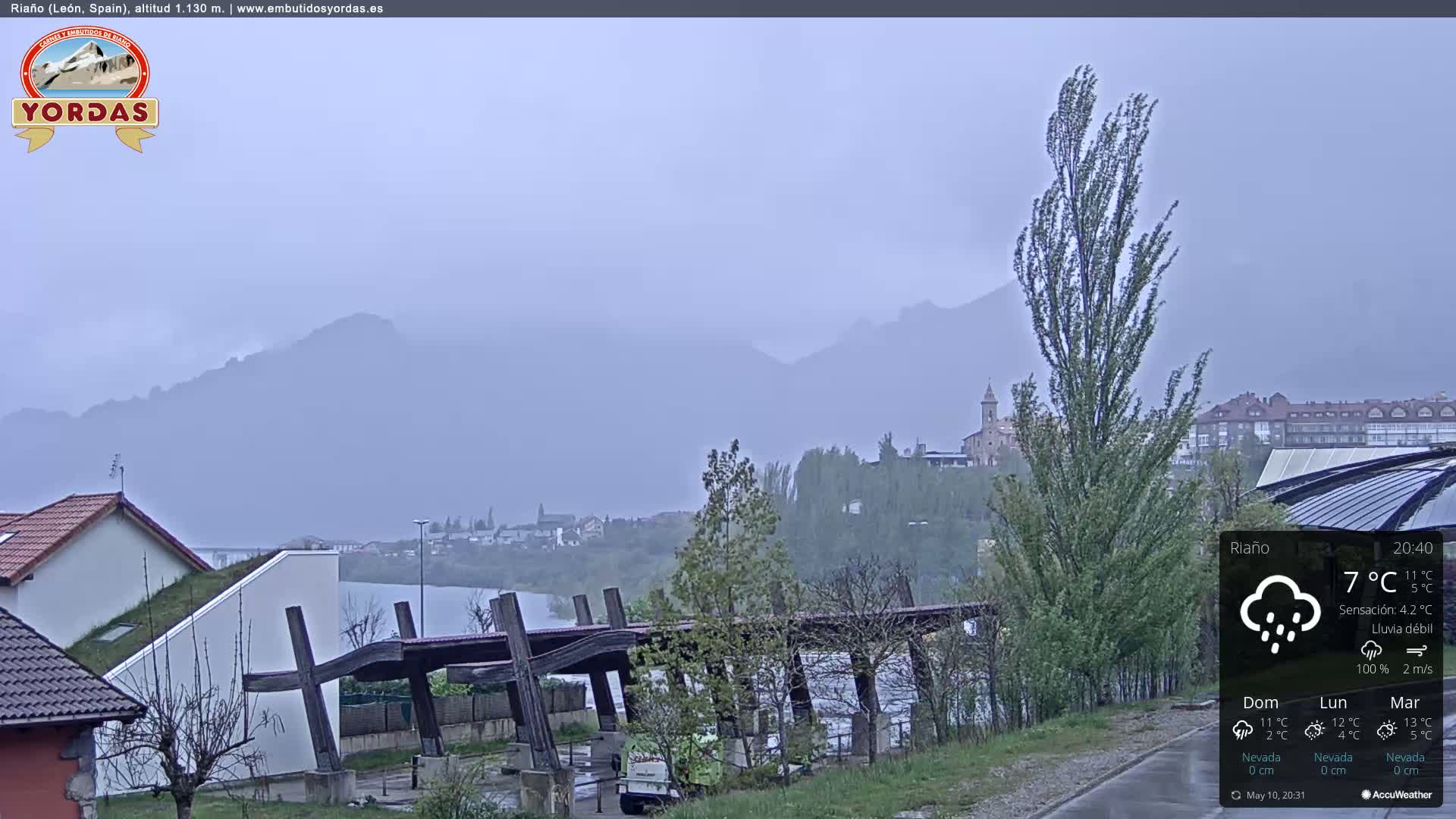 A misty, rainy scene overlooks a lake and distant mountains, with houses and trees in the foreground.