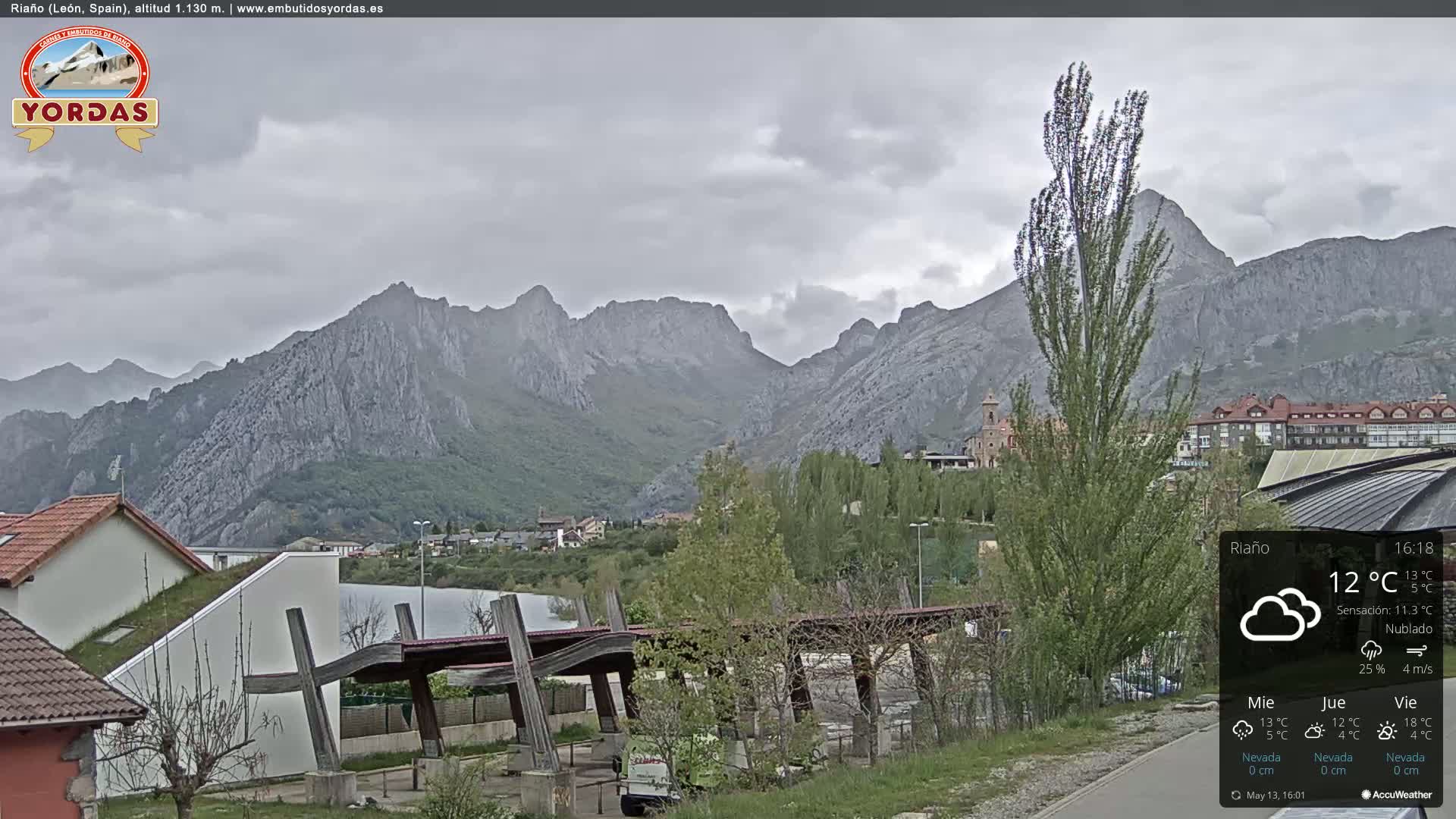 A cloudy view of a town nestled in a valley, with imposing mountains in the background.