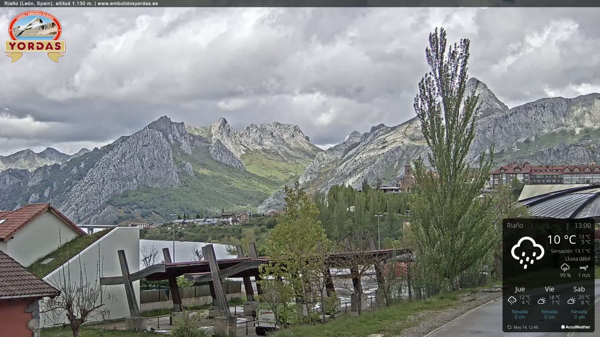 A town nestled in a valley surrounded by rocky mountains under a cloudy sky with light rain.