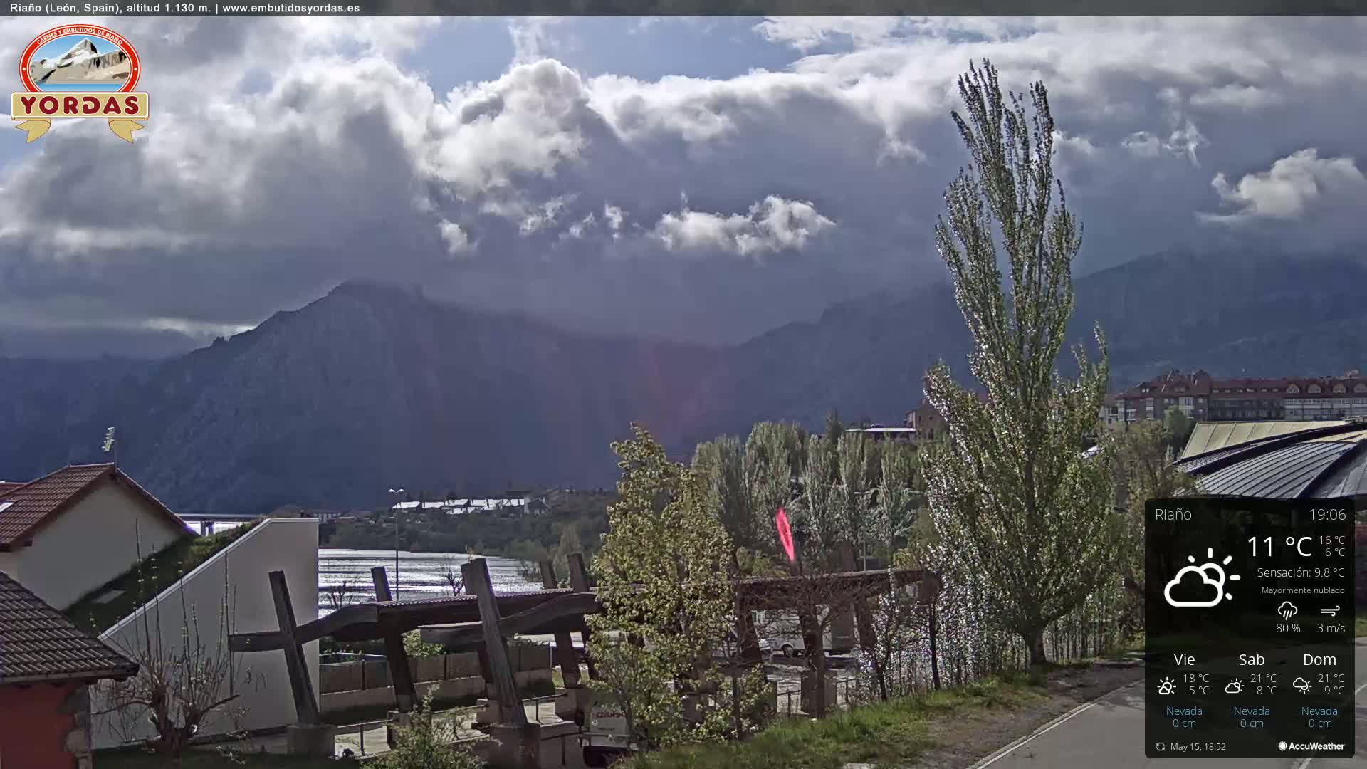 A mostly cloudy view of a town nestled in a valley, with mountains in the background.