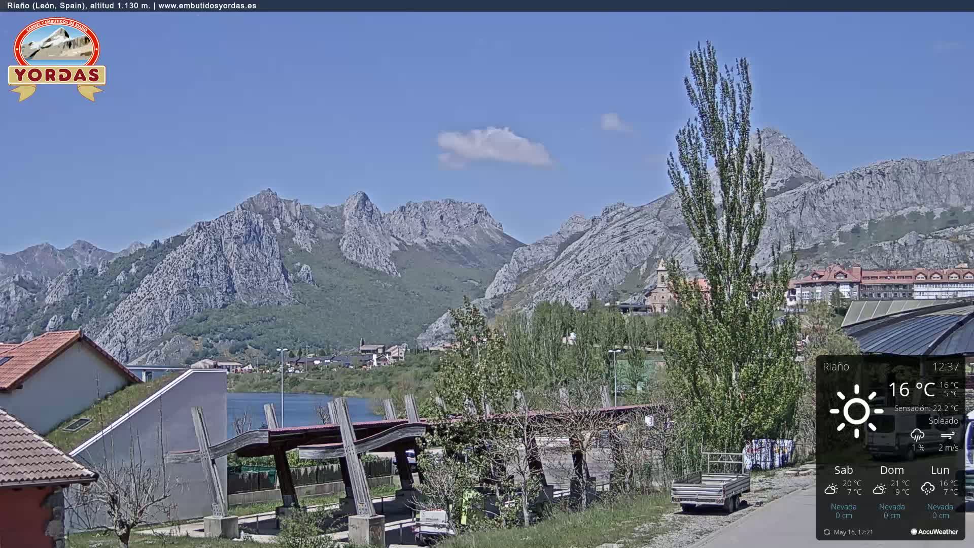 A sunny day reveals a mountainous landscape with a town nestled below, a calm lake, and a modern structure in the foreground.