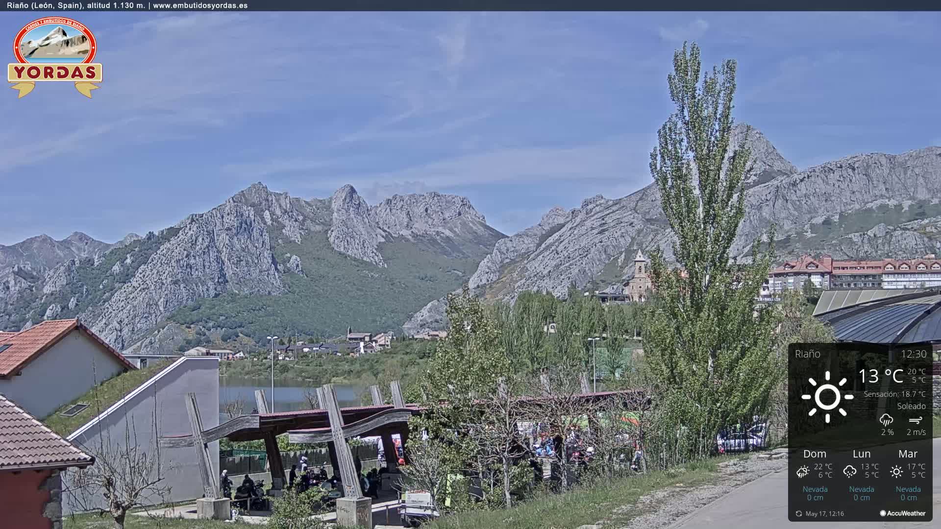 A sunny view of a town nestled beside a lake and surrounded by large, rocky mountains.