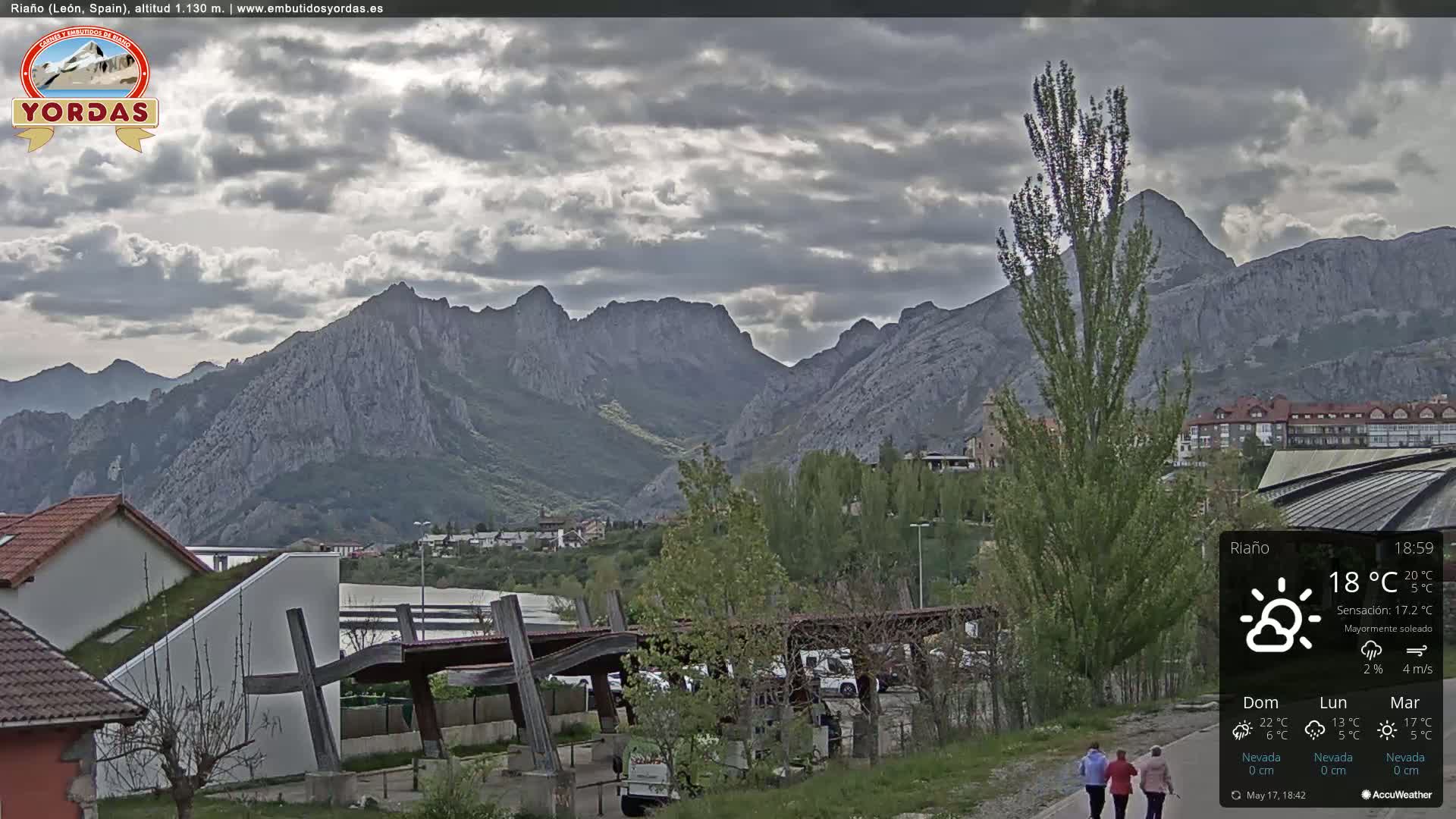 A partly sunny view of a town nestled at the base of a mountain range under a mostly cloudy sky.