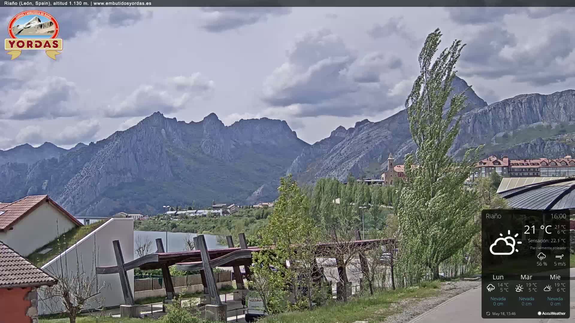A partly sunny view of a town nestled in a valley, with a mountainous backdrop.