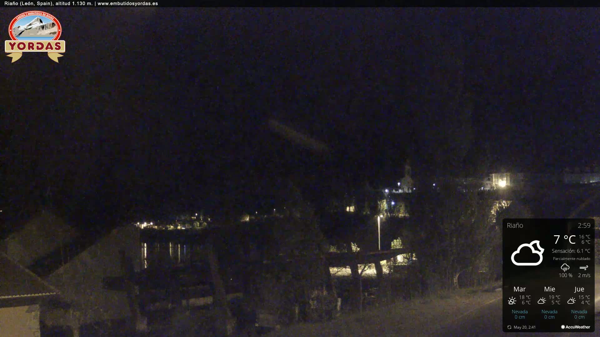A nighttime view of a town by a body of water under partly cloudy skies.
