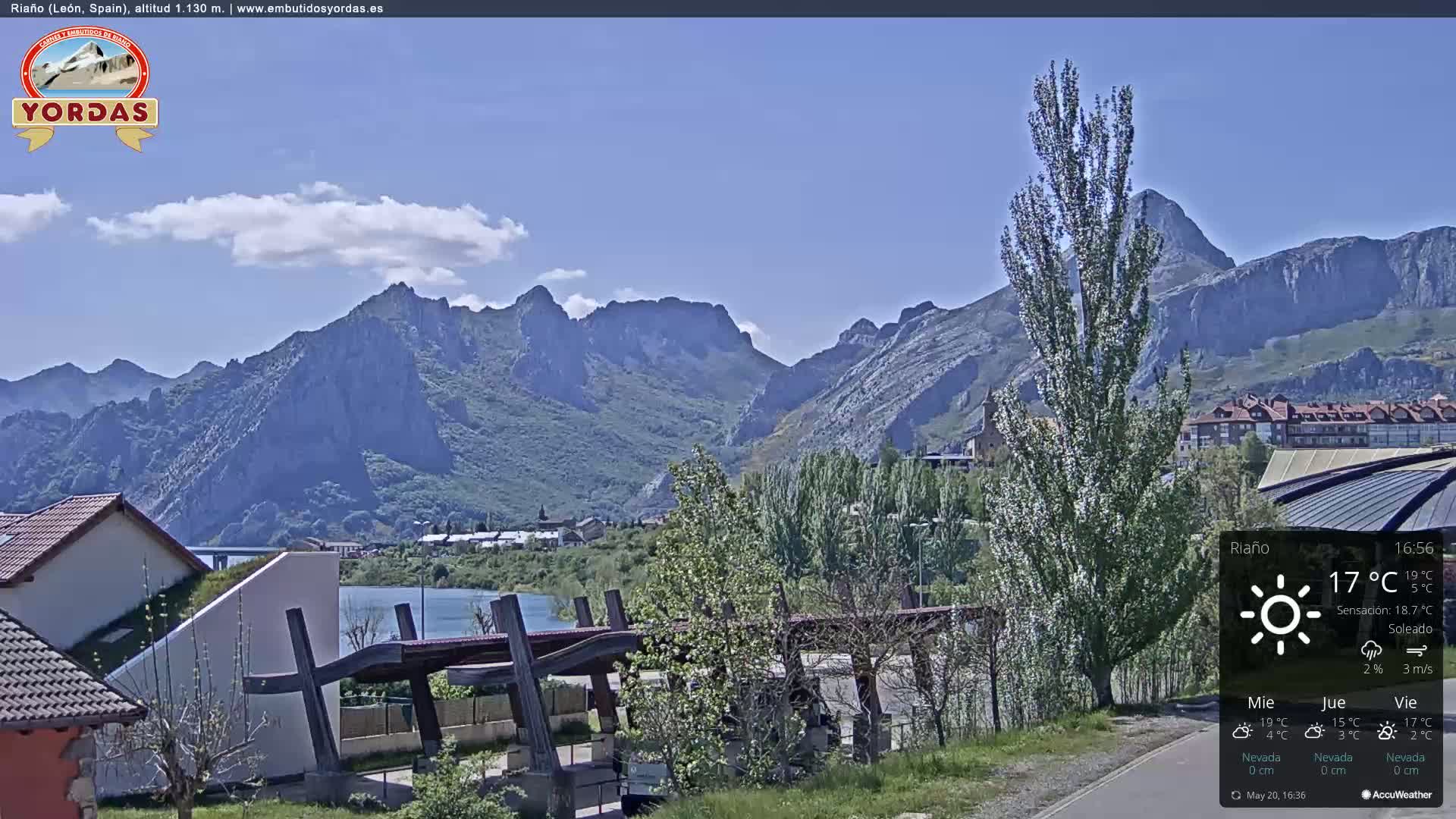 A sunny view of a town nestled beside a lake, with large mountains in the background.