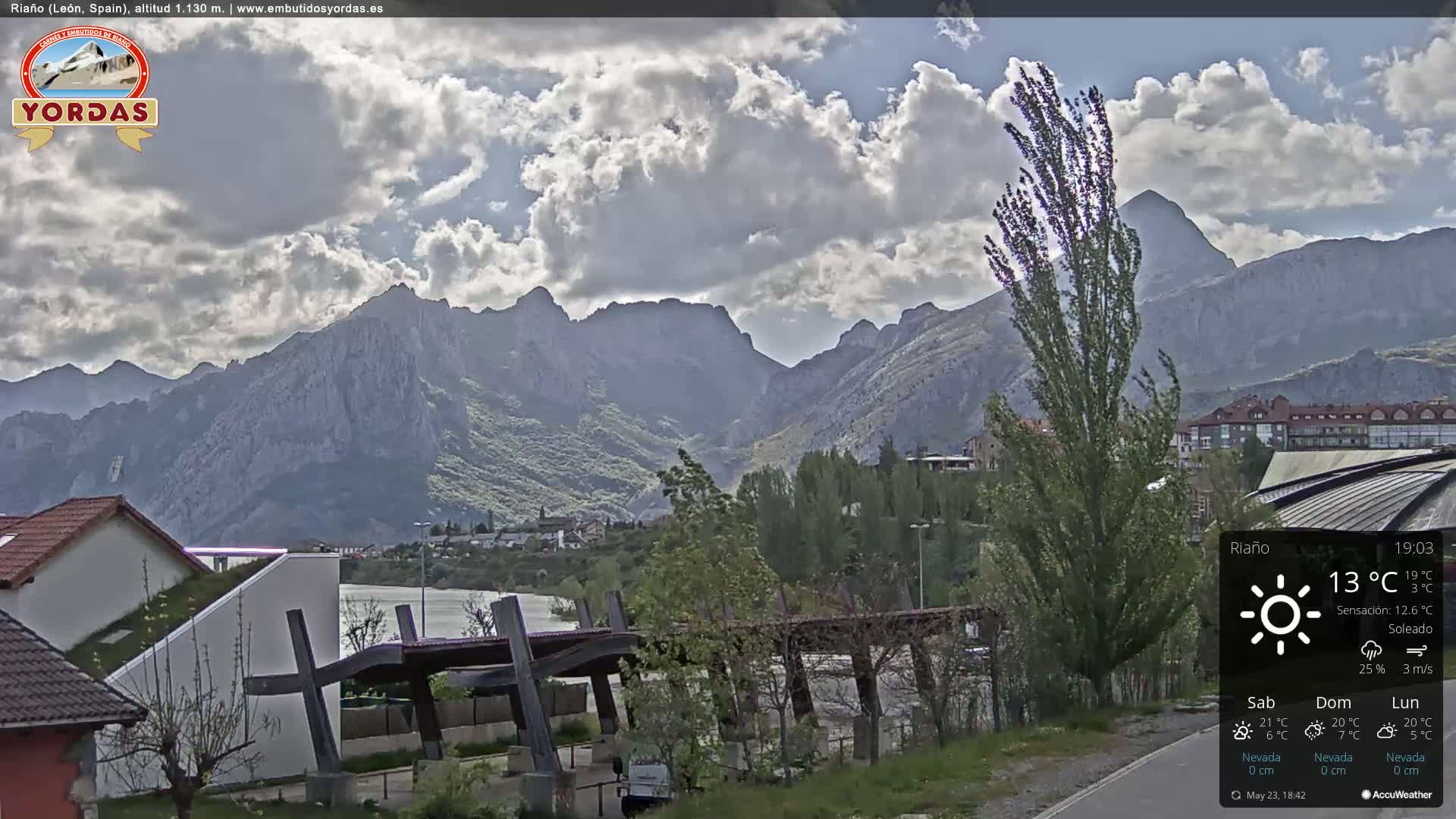 A partly cloudy day with mountains in the background, a town nestled at the foot of the mountains, and a modern structure in the foreground.