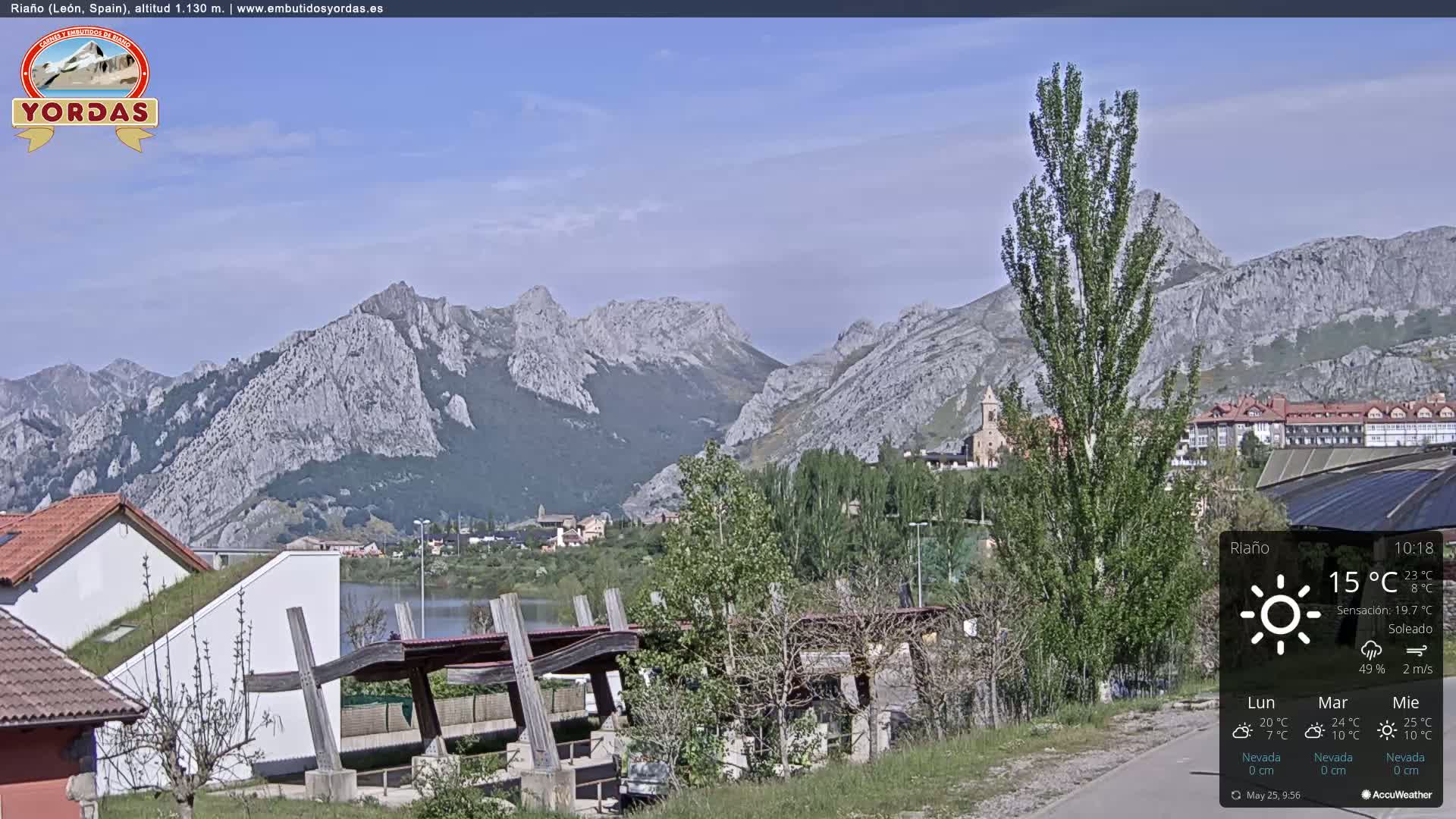 A sunny day reveals a town nestled beside a lake and mountains, with a wooden structure in the foreground.