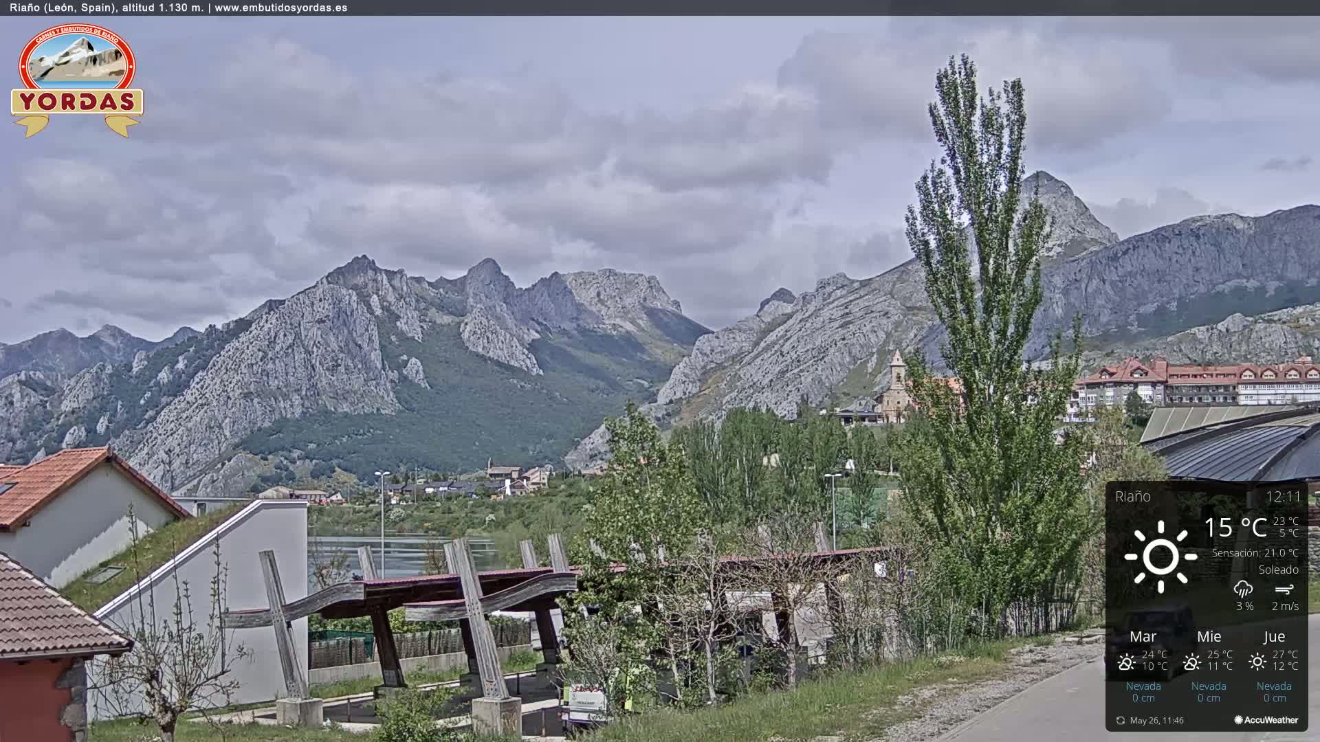 A partly cloudy day reveals a mountainous landscape with a town nestled in the valley below, and modern buildings near a wooden structure.