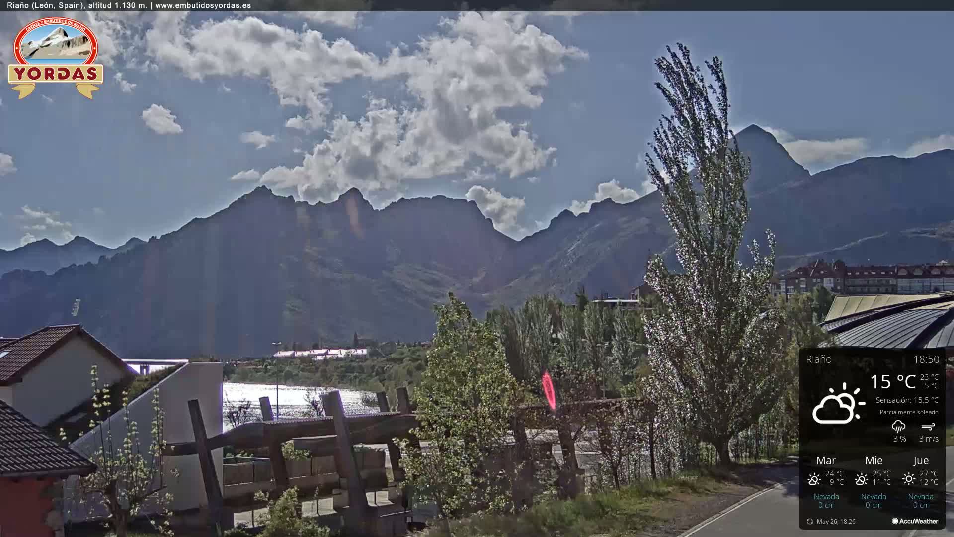A partly sunny view of a town nestled at the base of a mountain range under a mostly clear sky.