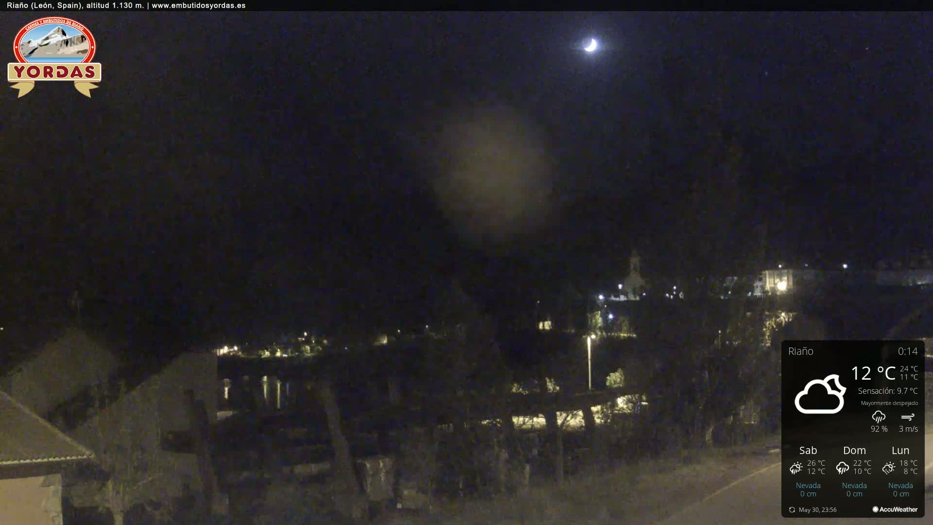 A nighttime view of a town under a mostly clear sky with a crescent moon visible.