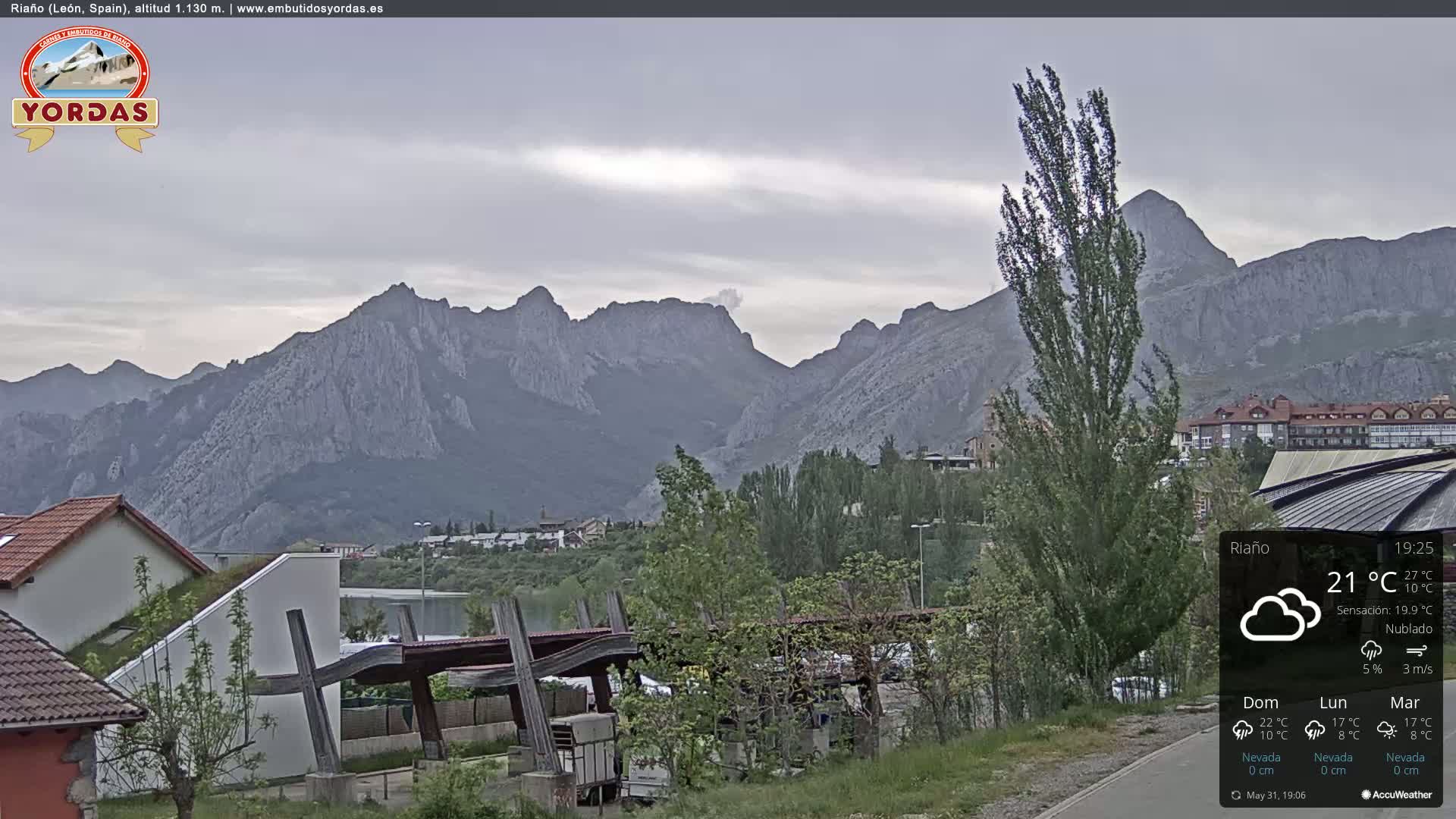A cloudy view of a town nestled at the base of a large mountain range.