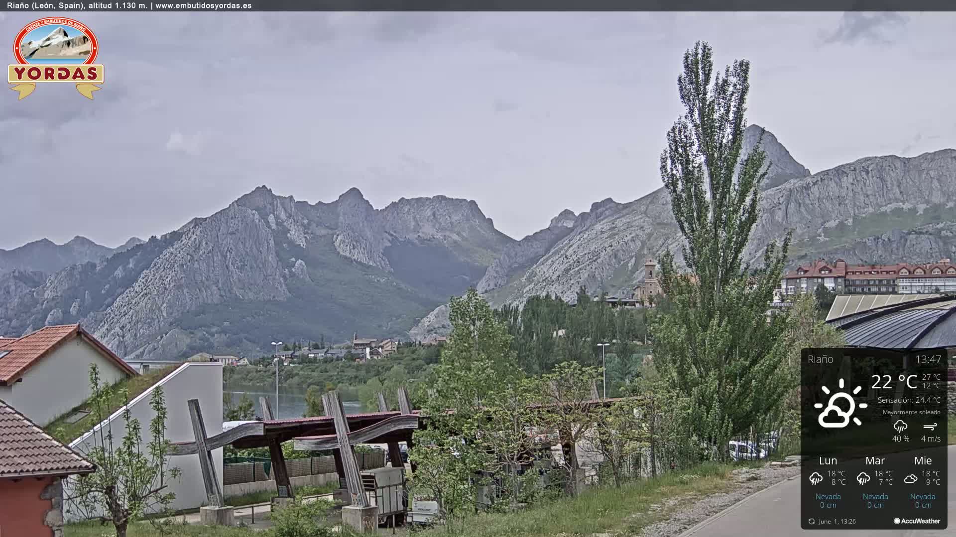A mostly sunny view of a town nestled in a valley, with a mountain range in the background.