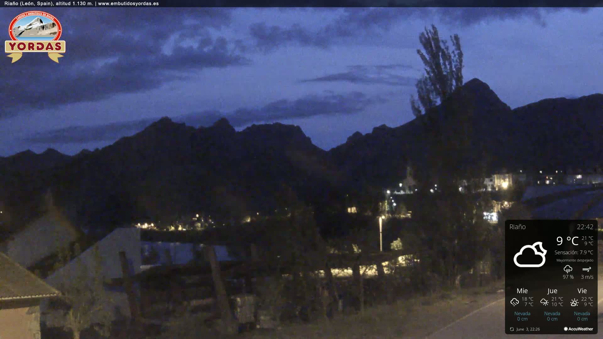 A nighttime view of a small town nestled in a valley between dark mountains under a mostly clear sky.