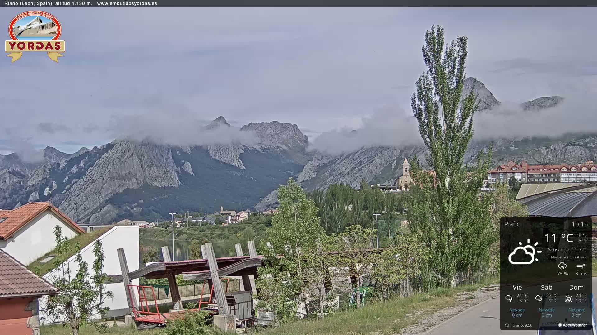 A partly cloudy day reveals a town nestled in a valley surrounded by misty mountains.