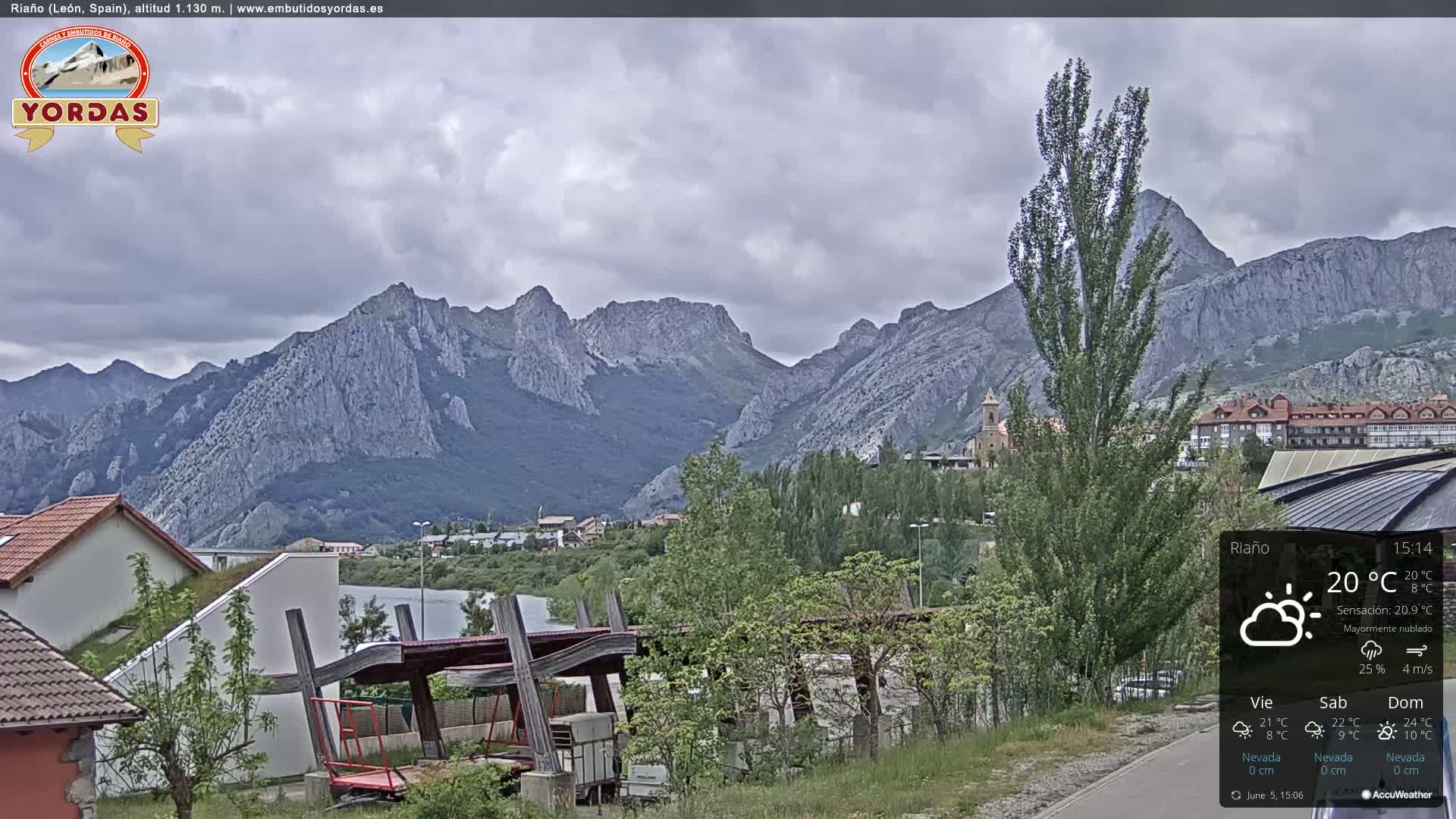 A town nestled at the base of a mountain range under a mostly cloudy sky.