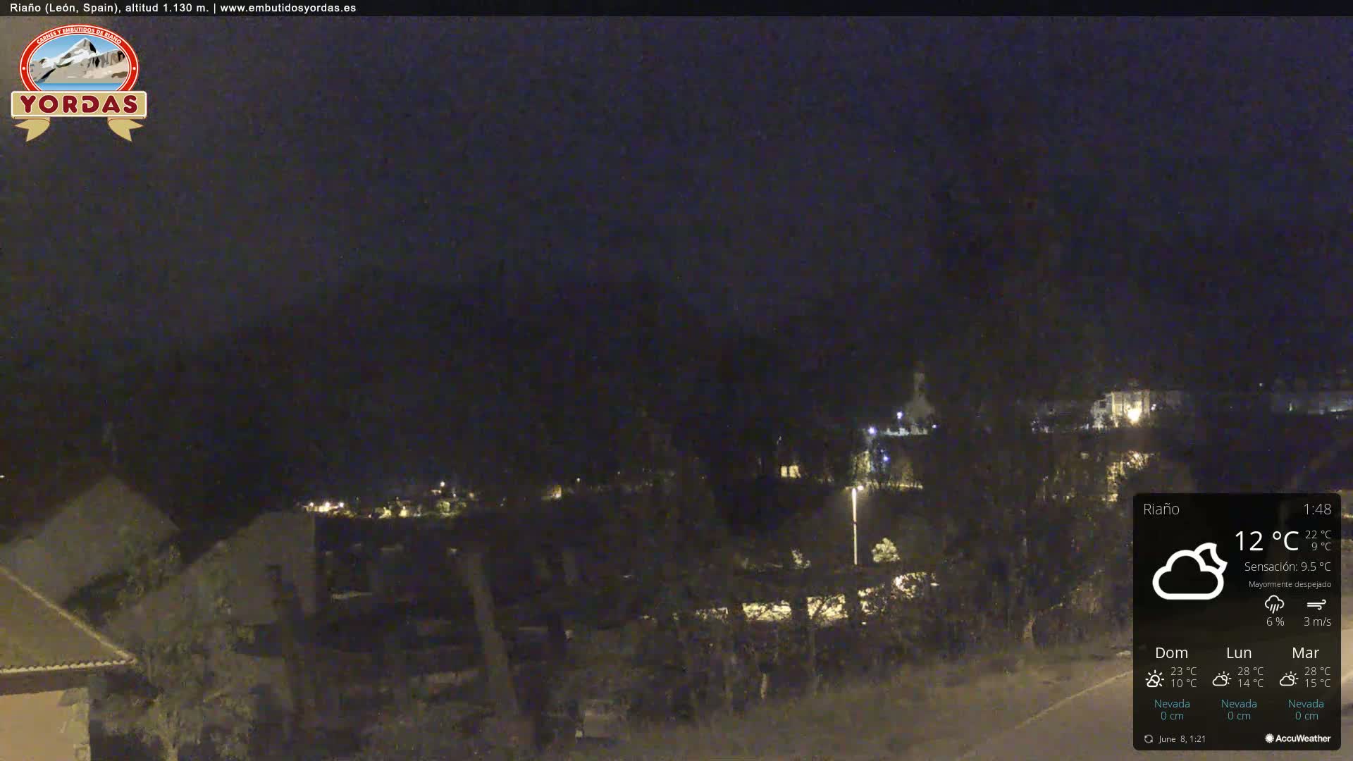 A nighttime view of a sparsely lit town nestled among dark hills under a mostly clear sky.