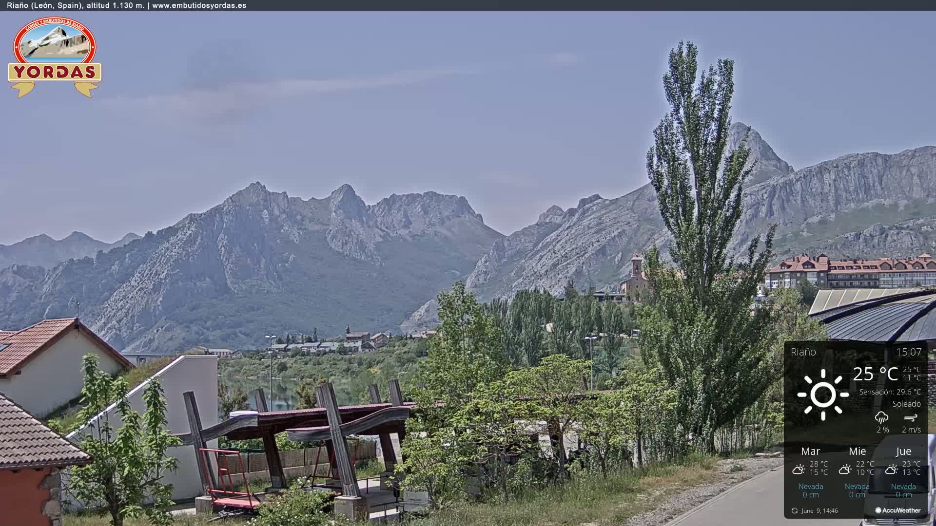 A sunny view of a town nestled in a valley, with a mountain range in the background.