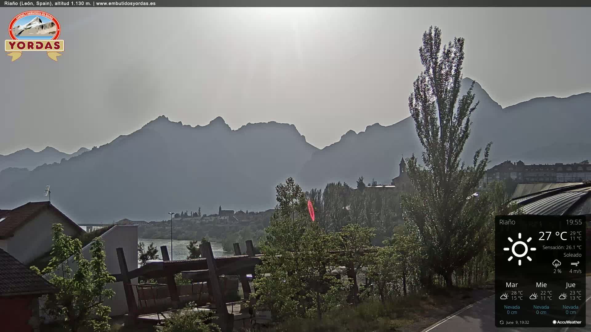 A hazy, sunny view of a town nestled beside a river, with mountains in the background.