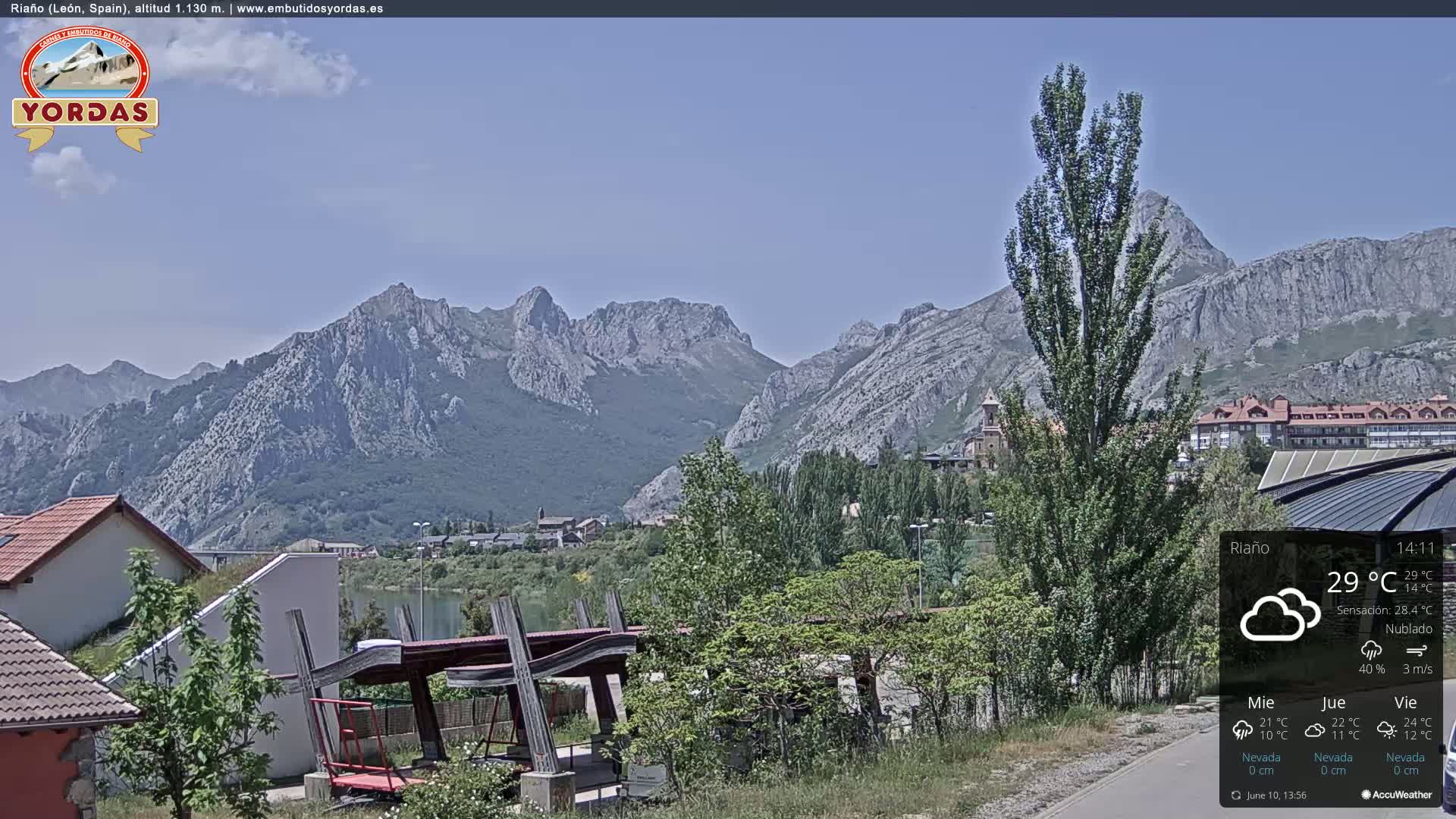 A partly cloudy day shows a view of a town nestled at the base of a large mountain range.