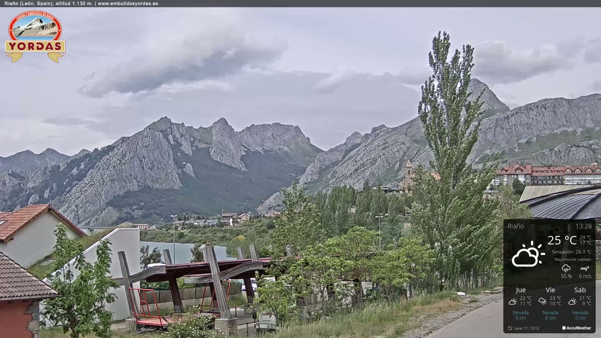 A mostly cloudy day reveals a mountainous landscape with a town nestled at the base of the mountains and a playground visible in the foreground.